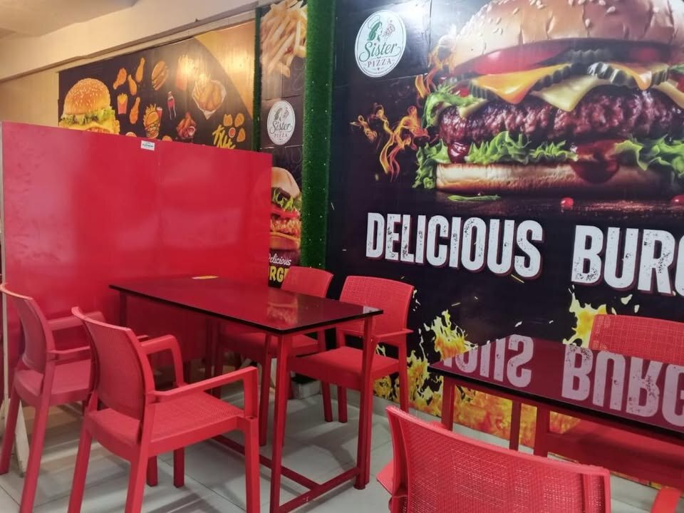 Inside Sister Pizza — red tables and chairs beside the burger mural at Al Noor Plaza
